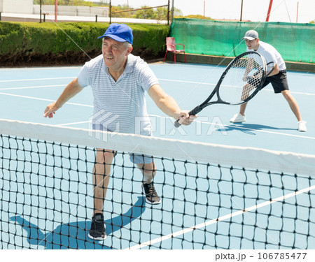Man with black racket playing match in open behind net court outdoors. Man with black racket playing match in open behind net court outdoors. 106785477
