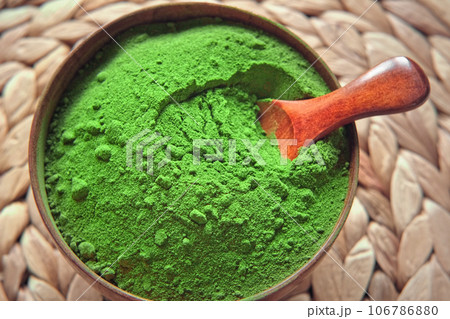 Wooden spoon with powdered matcha tea in a bowl spinning on natural background. Matcha powder. Top view, Closeup. Finely ground green powder. Japanese culture. Healthy eating with high antioxidants. 106786880