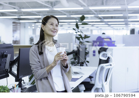 オフィスのデクスに腰掛けてタンブラーを持つシニアビジネスウーマンのポートレート 106790594