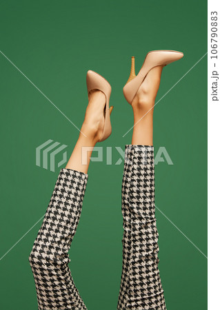 Female legs in heeled beige shoes and in checkered pants over green background. Smart casual, business style Female legs in heeled beige shoes and in checkered pants over green background. Smart casual, business style 106790883