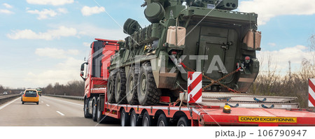 Back view armoured personnel carrier stryker with air defense system trailer hauler carrier truck drive military convoy highway road. US troops moving reloceation force reinforcement eastern Europe Back view armoured personnel carrier stryker with air defense system trailer hauler carrier truck drive military convoy highway road. US troops moving reloceation force reinforcement eastern Europe 106790947