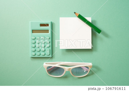 Green calculator and white memo note pad, colored pencil, eyeglasses on green background. top view 106791611