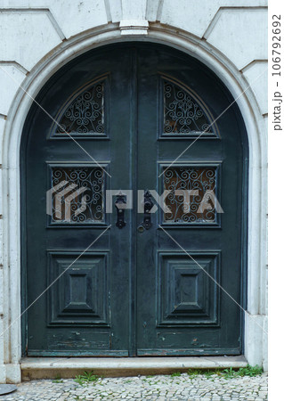 Beautiful big old ancient blue wooden arched door of stone building house decorated with forgings carvings ornaments. Beautiful big old ancient blue wooden arched door of stone building house decorated with forgings carvings ornaments. 106792692