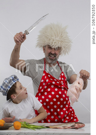 Georgian cheerful grandfather in a papakha hat teaches his grandson how to cook chicken. Master class in cooking. 106792850