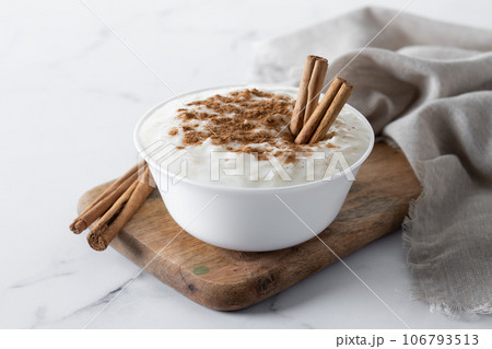 Arroz con leche. Rice pudding with cinnamon in clay bowl on white marble Arroz con leche. Rice pudding with cinnamon in clay bowl on white marble 106793513