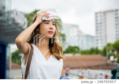 Angry female having sunstroke skin damage from sun UV city air pollution outside on street, Overheating Asian beautiful business woman drying sweat her face with cloth in warm summer day hot weather 106793957