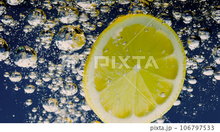 Underwater lemon slice in soda water or lemonade with bubbles. Refreshing soda tonic fizzy cocktail. Close up of lemons and ice cubes in glass. Lime in splashing sparkling water cold drink beverage. 106797533