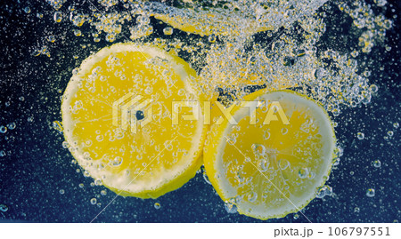 Underwater lemon slice in soda water or lemonade with bubbles. Refreshing soda tonic fizzy cocktail. Close up of lemons and ice cubes in glass. Lime in splashing sparkling water cold drink beverage. 106797551