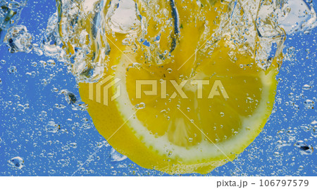 Underwater lemon slice in soda water or lemonade with bubbles. Refreshing soda tonic fizzy cocktail. Close up of lemons and ice cubes in glass. Lime in splashing sparkling water cold drink beverage. Underwater lemon slice in soda water or lemonade with bubbles. Refreshing soda tonic fizzy cocktail. Close up of lemons and ice cubes in glass. Lime in splashing sparkling water cold drink beverage. 106797579