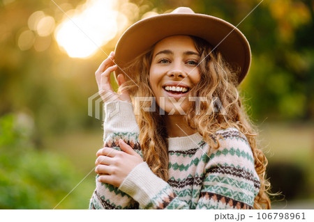 Happy woman in stylish sweater and hat outdoors in autumn park on plaid. Woman enjoys autumn nature. Happy woman in stylish sweater and hat outdoors in autumn park on plaid. Woman enjoys autumn nature. 106798961