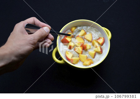 oatmeal cooked in milk with pieces of ripe peach in a bowl on a black background 106799381
