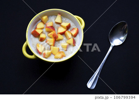 oatmeal cooked in milk with pieces of ripe peach in a bowl on a black background oatmeal cooked in milk with pieces of ripe peach in a bowl on a black background 106799394
