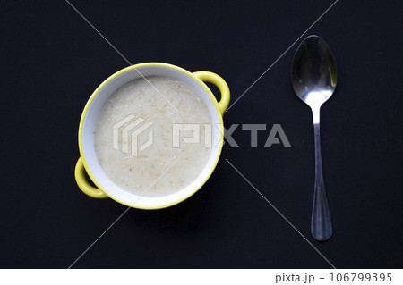 bowl with oatmeal cooked in milk and spoon on a black background bowl with oatmeal cooked in milk and spoon on a black background 106799395