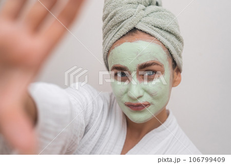 Glowing Self-Portrait: Donning a bathrobe, she grins at the camera, clay mask enhancing her selfie with radiant joy. Glowing Self-Portrait: Donning a bathrobe, she grins at the camera, clay mask enhancing her selfie with radiant joy. 106799409