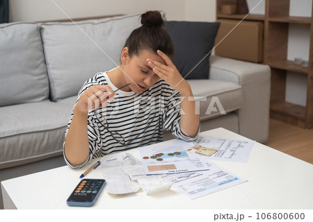 Woman carefully examines papers with prices of utilities for month lady accountant counts total amount holding head with hand sitting at coffee table in light flat 106800600
