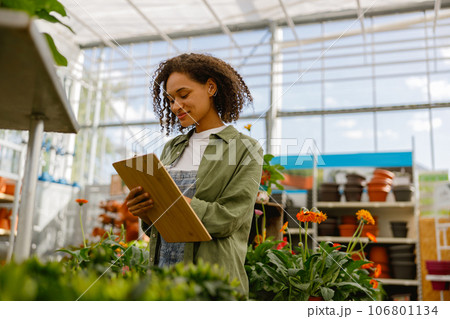 Woman garden center worker making notes in clipboard while standing in greenhouse 106801134