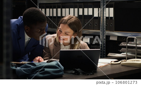 Female and male private detectives collaborate in incident room, analyzing evidence, conducting research, and sharing intelligence to solve classified case. Police officers cross-checking documents. 106801273