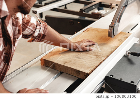 Close-up of carpenter's hands working with wood piece in a workshop 106803100