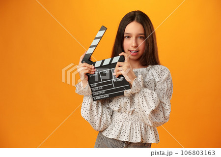 Happy smiling girl portrait holding clapper board on yellow background Happy smiling girl portrait holding clapper board on yellow background 106803163