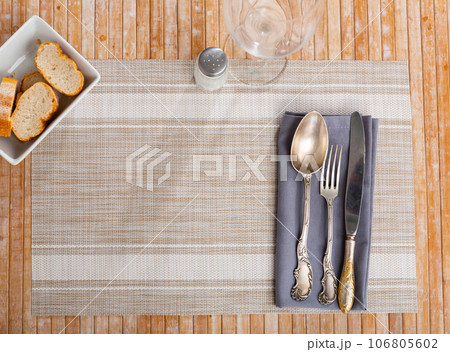 On cloth napkin with cutlery, complemented by glass for drinks and small plate with pieces of bread 106805602