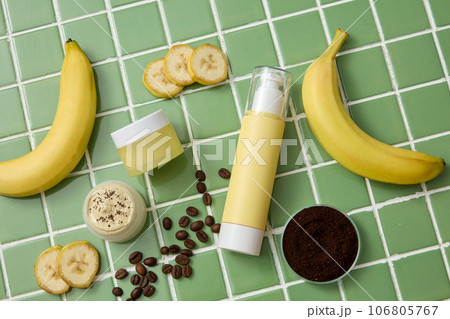 On the green ceramic background, set of cosmetic bottles displayed with ripe bananas, brown coffee beans and powder. Natural ingredients for cosmetics of skin care. Top view On the green ceramic background, set of cosmetic bottles displayed with ripe bananas, brown coffee beans and powder. Natural ingredients for cosmetics of skin care. Top view 106805767