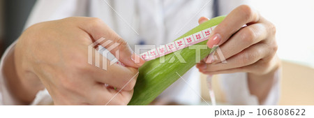 Doctor measures length of cucumber with measuring tape while sitting at table in medical clinic. 106808622
