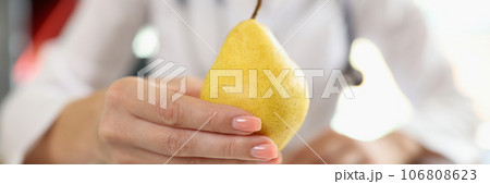 Close-up of pear in hand of nutritionist above medical office table. 106808623