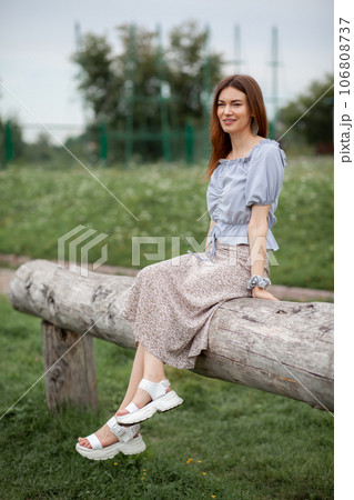 Smile of a young and beautiful girl with braces on her white teeth. A girl with long hair and a dress poses in the park. Straightening crooked teeth using a braces system. Smile of a young and beautiful girl with braces on her white teeth. A girl with long hair and a dress poses in the park. Straightening crooked teeth using a braces system. 106808737