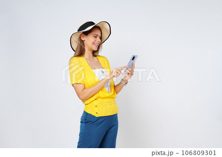 Young woman holding cell phone and smiling wearing a sun hat and sunglasses isolated on white background. Young woman holding cell phone and smiling wearing a sun hat and sunglasses isolated on white background. 106809301