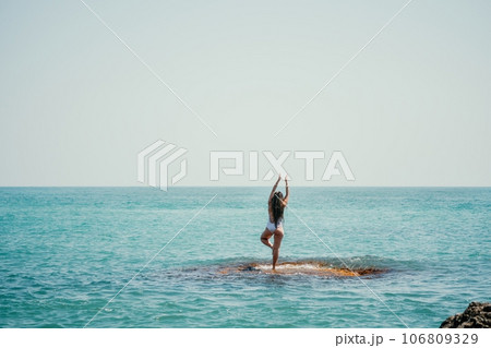 Woman sea yoga. Back view of free calm happy satisfied woman with long hair standing on top rock with yoga position against of sky by the sea. Healthy lifestyle outdoors in nature, fitness concept 106809329