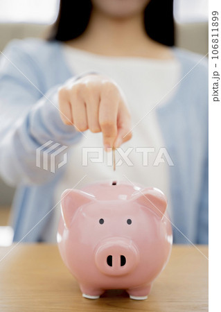 貯金箱にお金を入れる女性 106811899