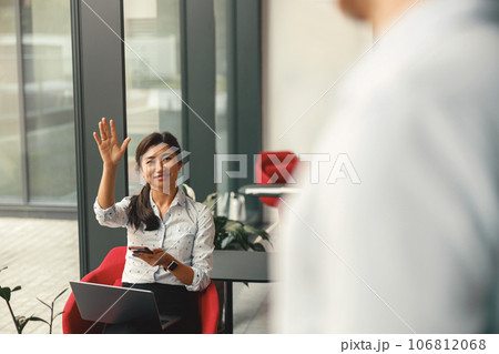 Female office worker waving Hi to her colleague during working day in coworking Female office worker waving Hi to her colleague during working day in coworking 106812068