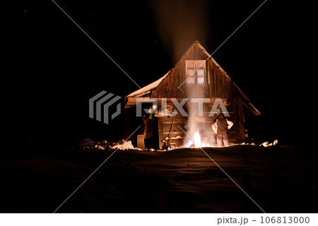Tourist heated by fire at winter near a wooden hut 106813000