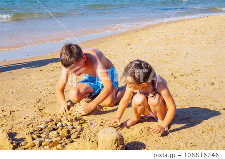 Portrait of preteen boy brother, little girl family sitting on beach seashore, playing with sand, building castles. 106816246