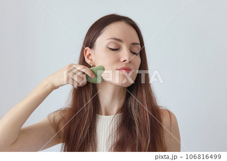 Close-up portrait of a beautiful girl, red-haired woman massaging her face with a stone scraper. Youth Corner 106816499