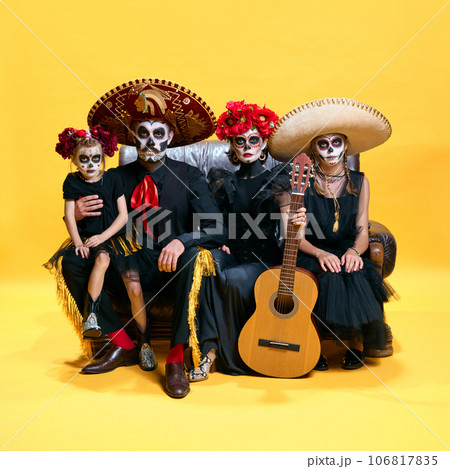 Adorable skeleton posing on yellow background. Happy mexicans family, parents and childrens with creative spooky makeup celebrating Halloween. Adorable skeleton posing on yellow background. Happy mexicans family, parents and childrens with creative spooky makeup celebrating Halloween. 106817835