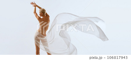 Back view. Cropped portrait of young sensual nudity female body, buttocks covering with white floating on air transparent fabric. 106817943