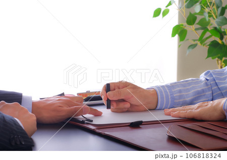 書類に印鑑を押す女性と促す男性の手元 106818324