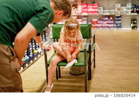 Little Girl and Father Shopping for Shoes in a Store. Child and Man Carefully Choose the Perfect Pair Together, Creating Cherished Memories and Strengthening Their Relationship as a Family 106820414