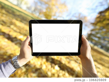 Man stands in autumn park and looks at tablet Man stands in autumn park and looks at tablet 106820809