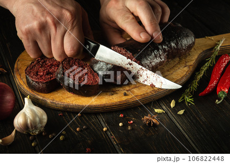 Slicing blood sausage by the hands of a chef on a cutting board. Cooking national dish on the kitchen table. 106822448