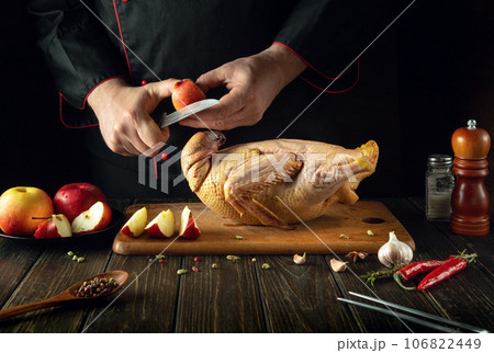 The chef cuts apples with a knife to add to raw duck before roasting in the oven. Cooking a national dish in the kitchen of a restaurant by the hands of a cook 106822449