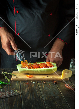 The cook adds a tomato to the zucchini. The concept of cooking a national stuffed squash boat or marrow in a restaurant kitchen. Free space for menu 106822465