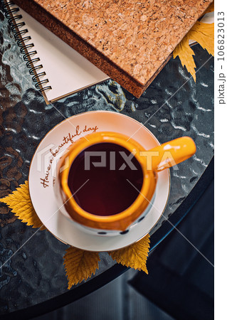 Autumn cozy still life on balcony, terrace. Fall cozy set with autumn fall leaves, cup of coffee or tea on brown books and notepads on balcony, terrace glass table. Relaxing still life concept. 106823013