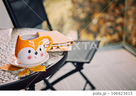 Autumn cozy still life on balcony, terrace. Fall cozy set with autumn fall leaves, cup of coffee or tea on brown books and notepads on balcony, terrace glass table. Relaxing still life concept. 106823015