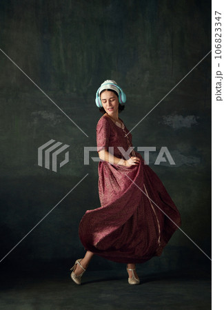 Medieval woman in elegant historical dress, maid listening to music in headphone and dancing against vintage green background Medieval woman in elegant historical dress, maid listening to music in headphone and dancing against vintage green background 106823347