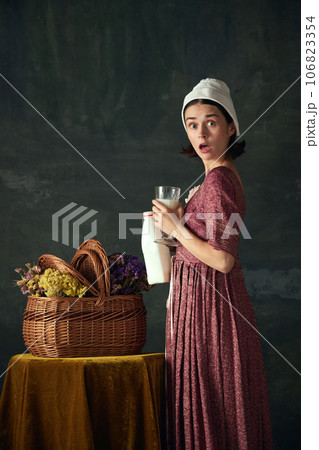 Shock and unexpected meeting. Emotive young woman, medieval maid with standing with milk against dark vintage background 106823354