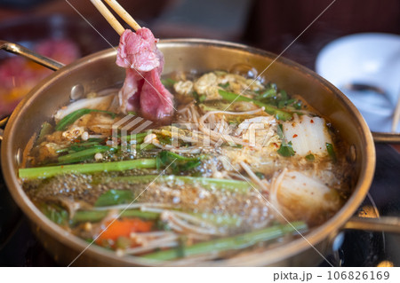 Chopstick holding sliced meat. hot pot with thick soup. Chopstick holding sliced meat. hot pot with thick soup. 106826169