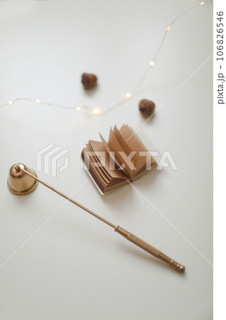 Home autumn composition with book and candle extinguisher in the interior of the room, on a blurred background with a garland. Home autumn composition with book and candle extinguisher in the interior of the room, on a blurred background with a garland. 106826546