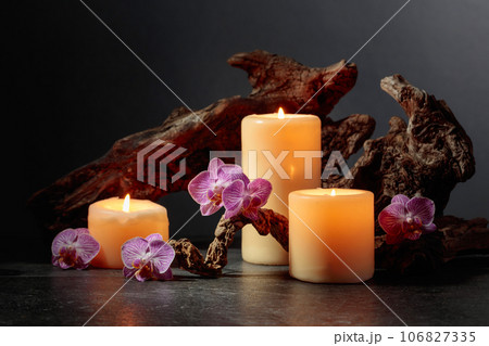 Orchid flowers, burning candles, and old wooden snags on a black background. 106827335
